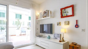 Een moderne woonkamer met een televisie, een bordje met de tekst 'Welcome to Sitges Home' en een foto in een rode lijst aan de muur.