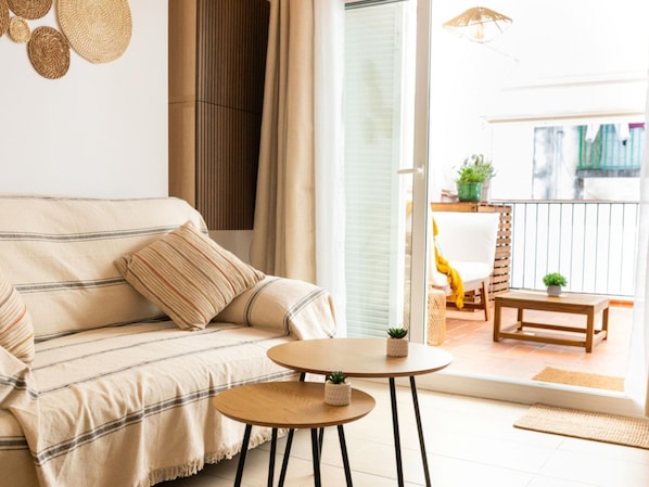 A living room with a sofa, a small round table, and a view of an outdoor balcony. - Cuban Green Terrace in Sitges (Sitges)