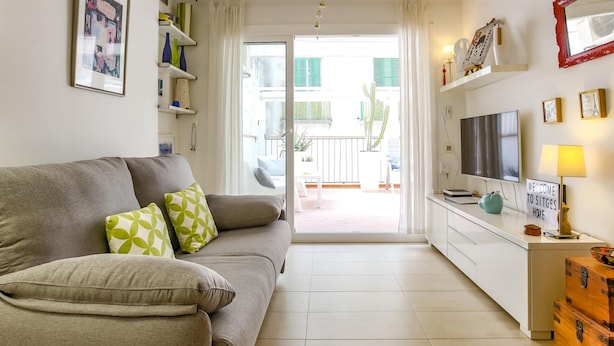 Een moderne woonkamer met een bank, televisie en een bordje met de tekst 'WELCOME TO SITGES HOME'.