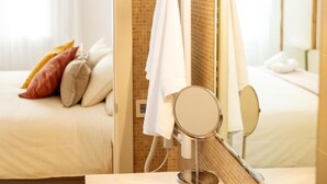A hotel bathroom with a shower, a mirror, and a bed with pillows.