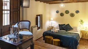 Una camera d'albergo con un letto, una sedia, un tavolo con un bicchiere, una lampada e piatti decorativi appesi al muro.