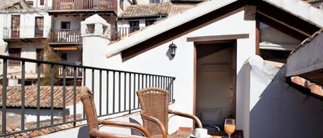 Een balkon met rieten meubels, een tafel met een croissant en sap, en uitzicht op traditionele gebouwen.