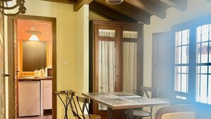 Zona pranzo con tavolo imbandito per quattro persone, circondato da sedie, un armadietto in legno e una finestra con tende.