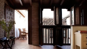 A room with a tiled floor, wooden ceiling beams, a brick wall, a wooden door, and a view of a tiled roof outside. - Apartamento Terraza Albaicin (Granada)