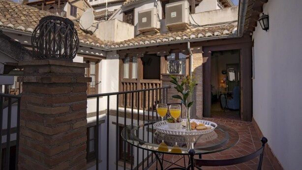 A glass table with a tray of food and drinks, a brick pillar, and a balcony with a view of buildings. - Apartamento Terraza Albaicin (Granada)