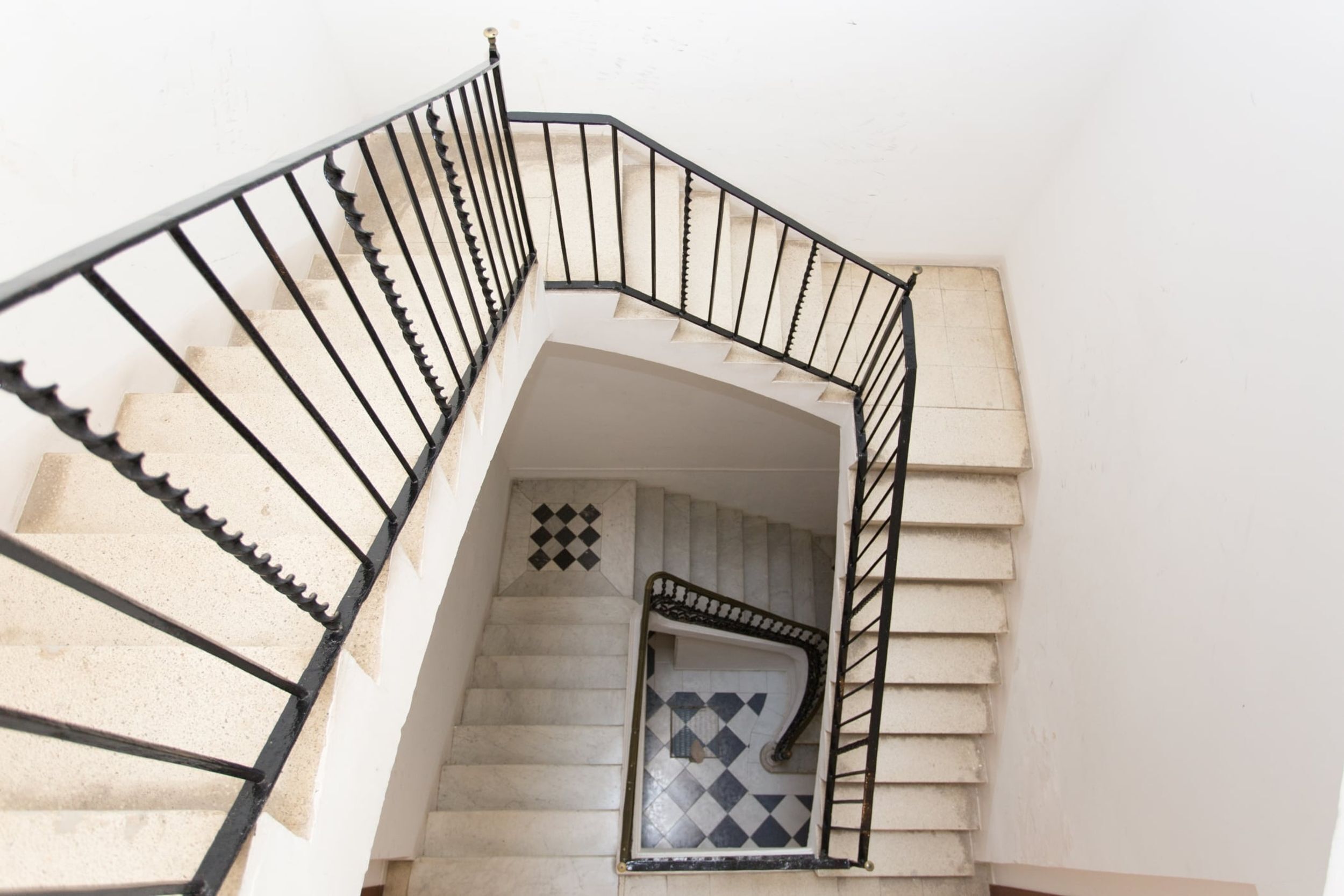 Una escalera de caracol con barandas negras y baldosas estampadas en el suelo.