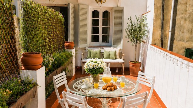 A glass-top table with white chairs, a small round table with a white tablecloth, and a window with shutters. - Apartamnet en el Centro de Sitges con Terraza (Sitges)