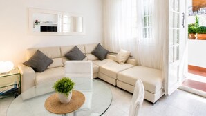A modern living room with a beige sectional sofa, a glass coffee table with a plant, and a large window with sheer curtains. - Apartamnet en el Centro de Sitges con Terraza (Sitges)