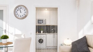 A modern living room with a sofa, a chair, a clock, and a laundry area with a washing machine. - Apartamnet en el Centro de Sitges con Terraza (Sitges)
