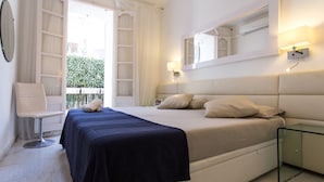 A bedroom with a bed, bedside table, chair, and a window with curtains. - Apartamnet en el Centro de Sitges con Terraza (Sitges)