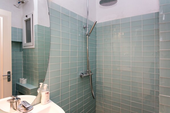 Un baño con ducha, espejo y lavamanos con artículos de aseo.