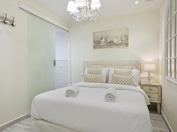 Un dormitorio ordenado con cama, mesita de noche, lámpara, candelabro y un cuadro en la pared.