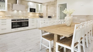 Een moderne keuken met witte kasten, een houten eettafel en witte stoelen.