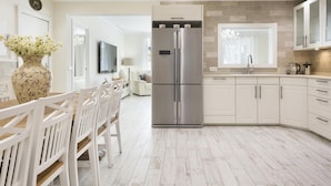 Een moderne keuken met witte kasten, een roestvrijstalen koelkast en een eethoek met witte stoelen en een bloevas.