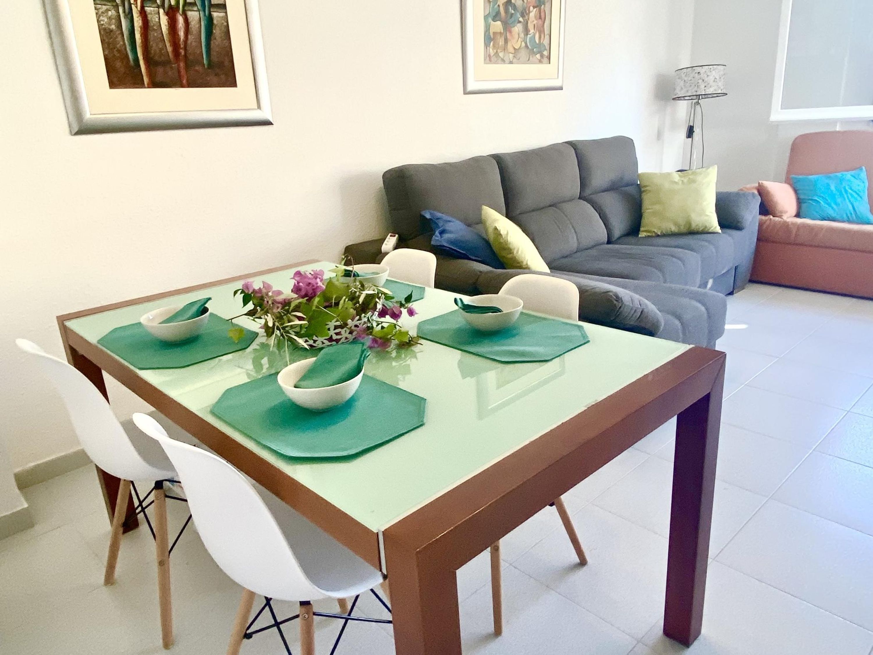 A dining area with a glass table, white chairs, and a vase of flowers.