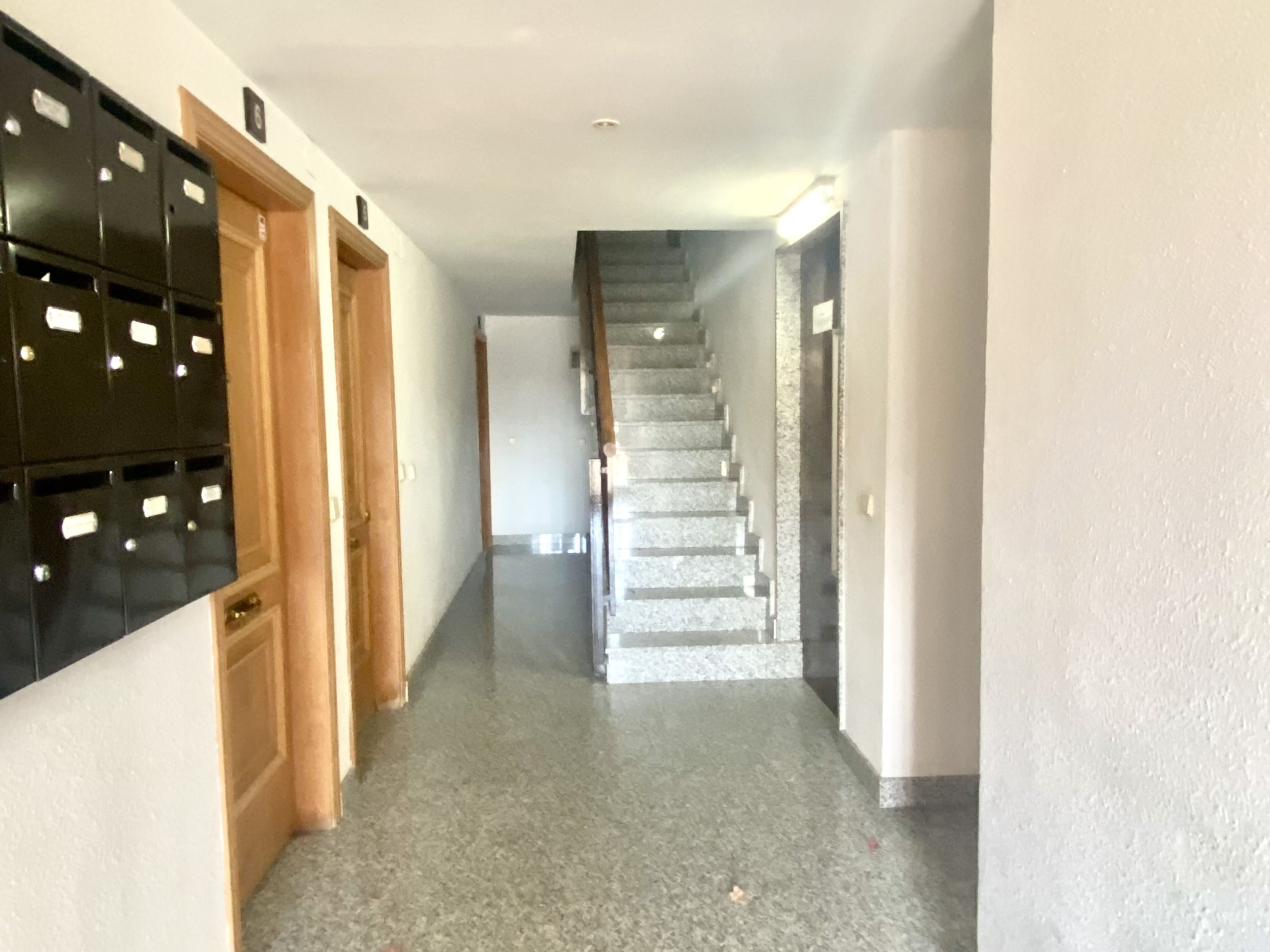 Un couloir avec un escalier, des meubles de rangement noirs et une porte en bois.