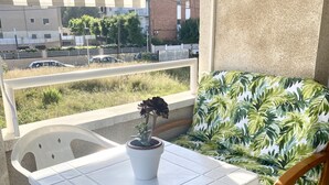 A balcony with a white table, a potted plant, and a chair with a leafy pattern. - Rental Unit in Calafell 3 Bedrooms 3 Beds 1 (El Vendrell)