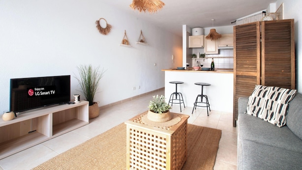 A modern living room with a flat-screen TV, a grey sofa, a wooden coffee table, and a kitchen in the background. - Luna de Opalo in Santiago del Teide (Santiago del Teide)