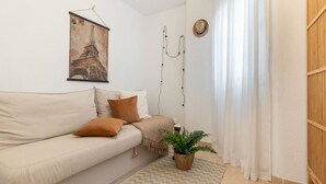 Un salon minimaliste avec un canapé, un luminaire suspendu, une plante en pot et un tableau représentant la Tour Eiffel, accroché au mur.