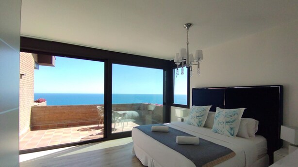 A bedroom with a large bed, a balcony with a view of the sea, and a modern chandelier. - Sitges Spaces Sea View Villa (Sitges)