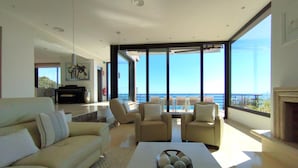 A modern living room with a large window overlooking the sea, a fireplace, and a billiards table. - Sitges Spaces Sea View Villa (Sitges)