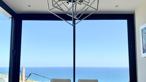 A dining area with a table and chairs, large windows with a view of the sea, and a pendant light fixture. - Sitges Spaces Sea View Villa (Sitges)