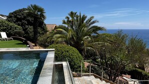 A swimming pool with clear water, surrounded by stone steps and palm trees, overlooking a body of water. - Sitges Spaces Sea View Villa (Sitges)