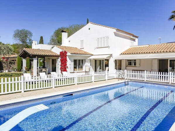 A swimming pool with a white fence, a white house with a tiled roof, and a garden with a pergola. - Casa Independiente con Jard n y Piscina Privada (Sant Pere de Ribes)