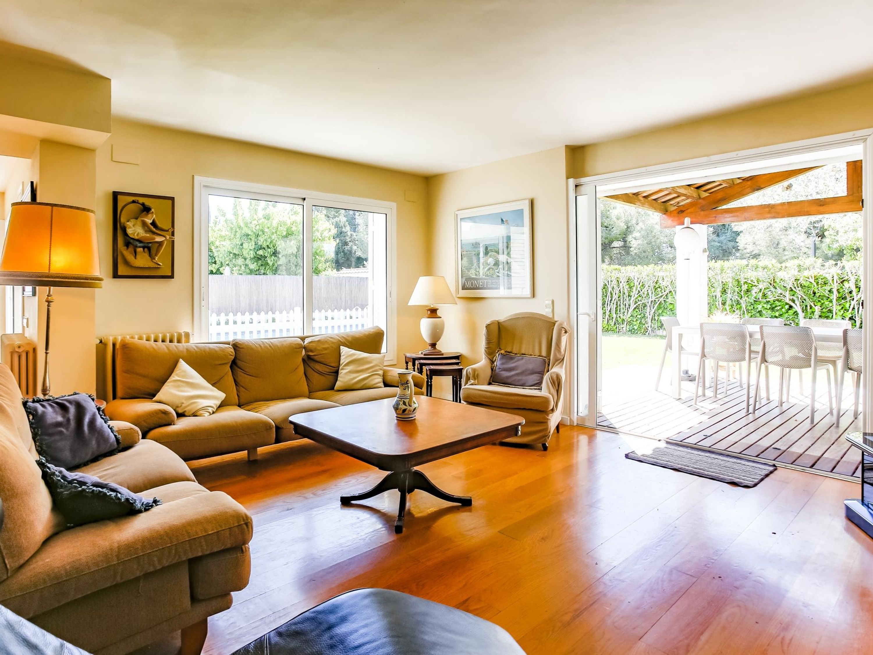 A living room with a sofa, coffee table, and armchairs. There is a window with a view of greenery outside.