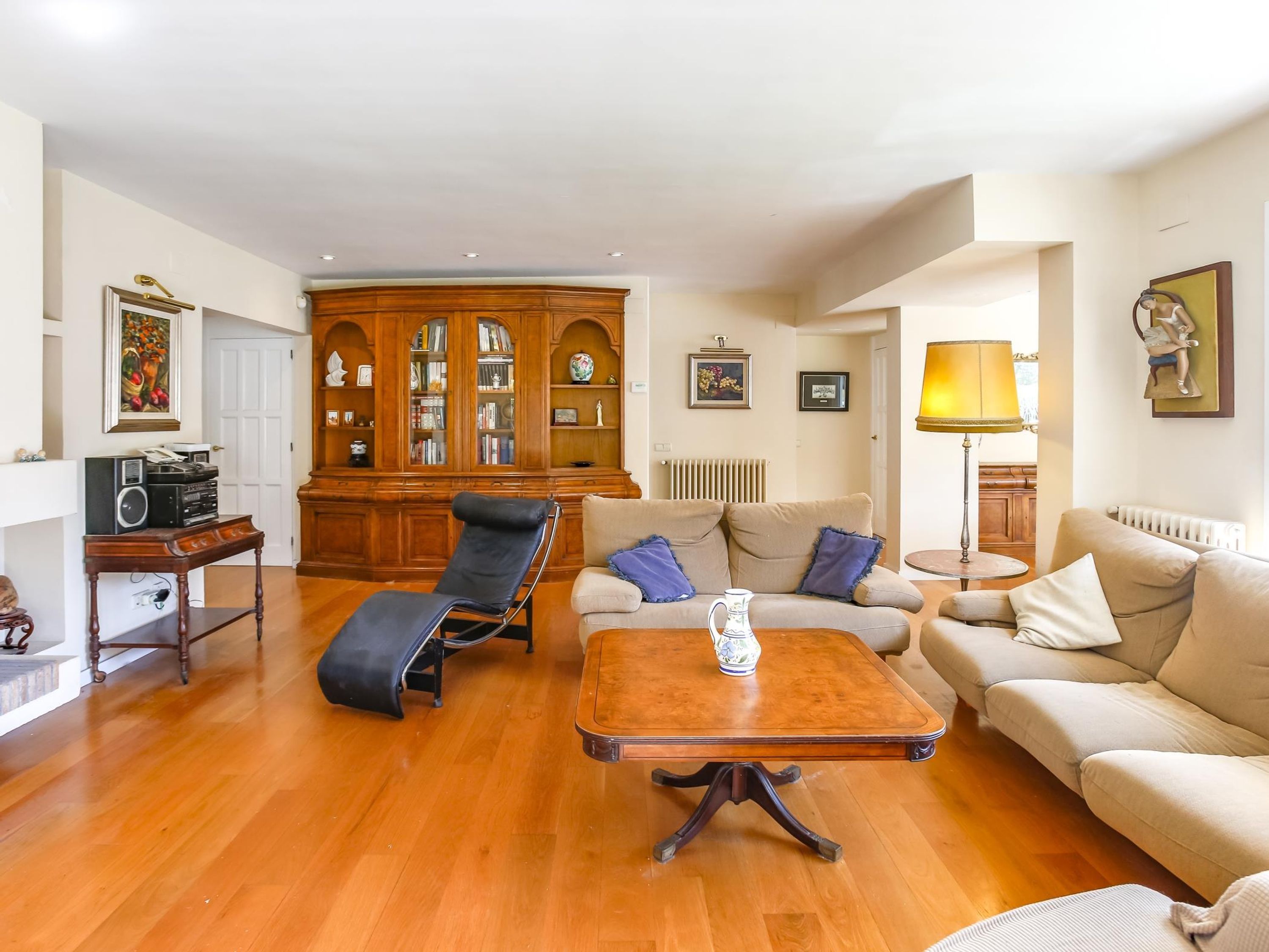 A living room with a wooden floor, a sofa, a lounge chair, a coffee table, a cabinet with glass doors, and a lamp.