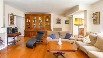 A living room with a wooden floor, a sofa, a lounge chair, a coffee table, a cabinet with glass doors, and a lamp.