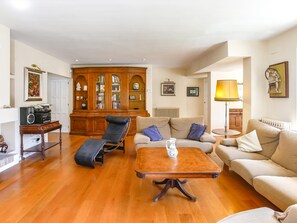 A living room with a wooden floor, a sofa, a lounge chair, a coffee table, a cabinet with glass doors, and a lamp. - Casa Independiente con Jard n y Piscina Privada (Sant Pere de Ribes)