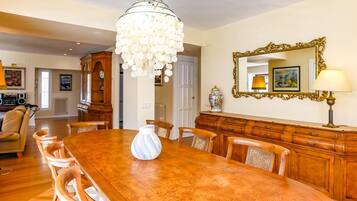 A dining room with a large wooden table, chairs, a chandelier, a mirror, and a cabinet.