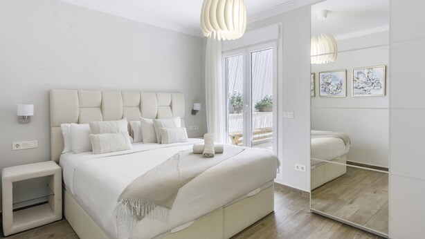 Un dormitorio moderno con una cama grande, mesitas de noche, un espejo y vistas al exterior.