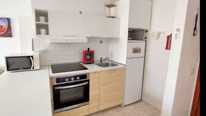 A compact kitchen with white cabinets, a microwave, a stove, and a refrigerator. - C Ntrico y a pie de Playa en los Cristianos (Arona)