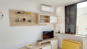 A modern, compact living space with a TV on a wooden stand, a small cabinet, and a window with curtains. - C Ntrico y a pie de Playa en los Cristianos (Arona)