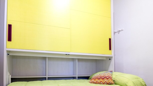 A room with a bed, a yellow wardrobe, and a white ceiling.