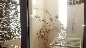 A view through a window of a room with a white bench, a potted plant, and a wall with a grid-like pattern.