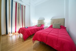 Ein Hotelzimmer mit zwei Betten, jeweils mit roter Bettdecke und Kopfteil. Zwei Nachttische mit Lampen stehen bereit, und der Raum hat Holzboden.