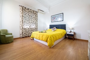 Ein Schlafzimmer mit einem Bett, einem Sessel, einem Nachttisch und einer Wand-Klimaanlage.