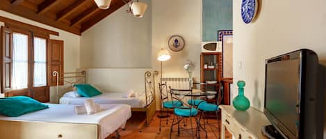 Una camera da letto con due letti, una televisione, un tavolo da pranzo con sedie e un angolo cottura.