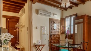 A dining area with a glass table and four teal chairs, a wooden cabinet, and an air conditioning unit on the wall. - Apartamento Rio Genil (Granada)