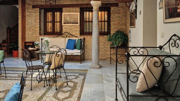 A cozy courtyard with a stone wall, a wooden ceiling, a metal bench, a sofa, and a table with chairs. - Apartamento Rio Genil (Granada)