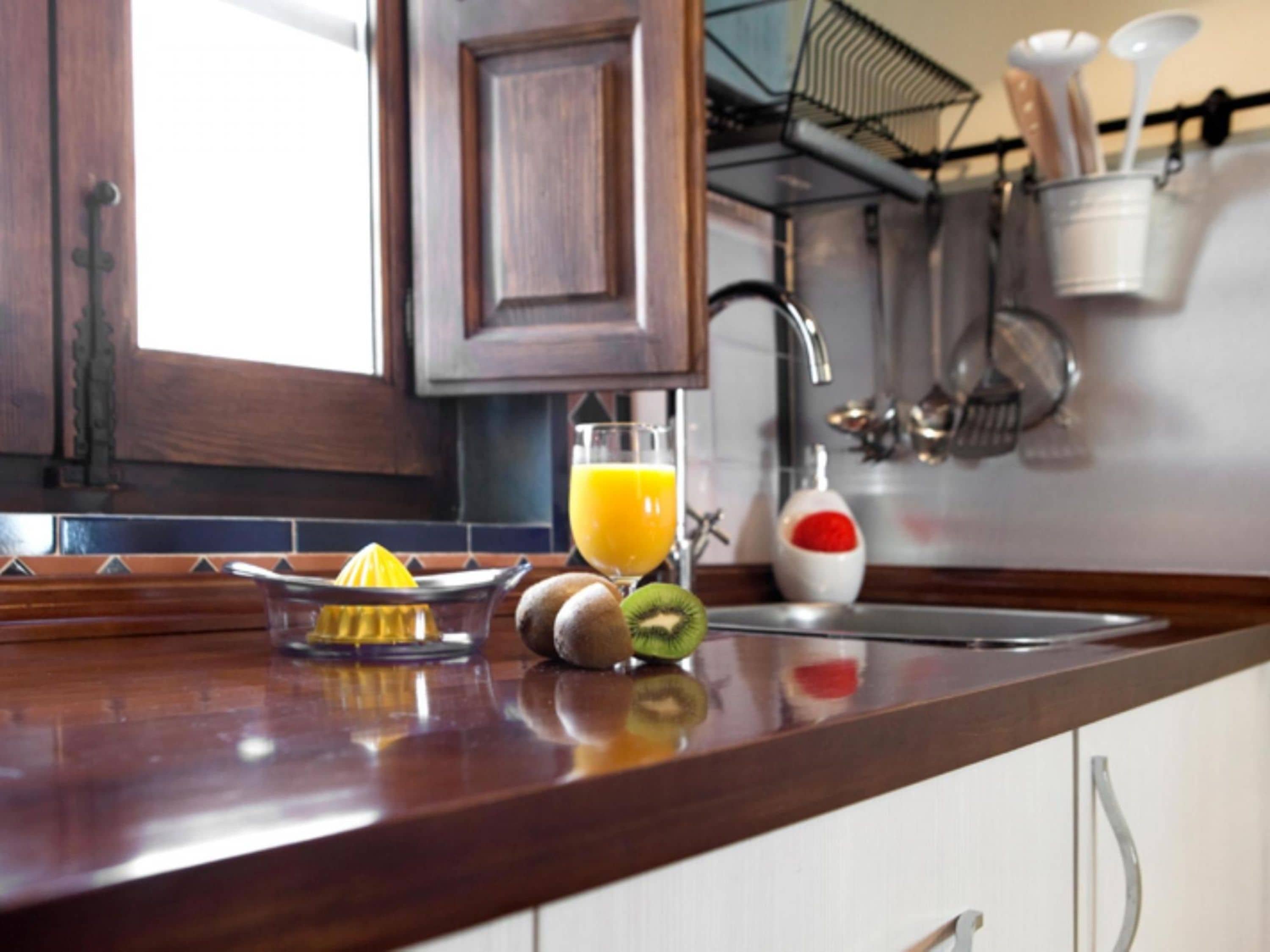 Una encimera de cocina con un extractor de zumo, un vaso de zumo de naranja y un kiwi.