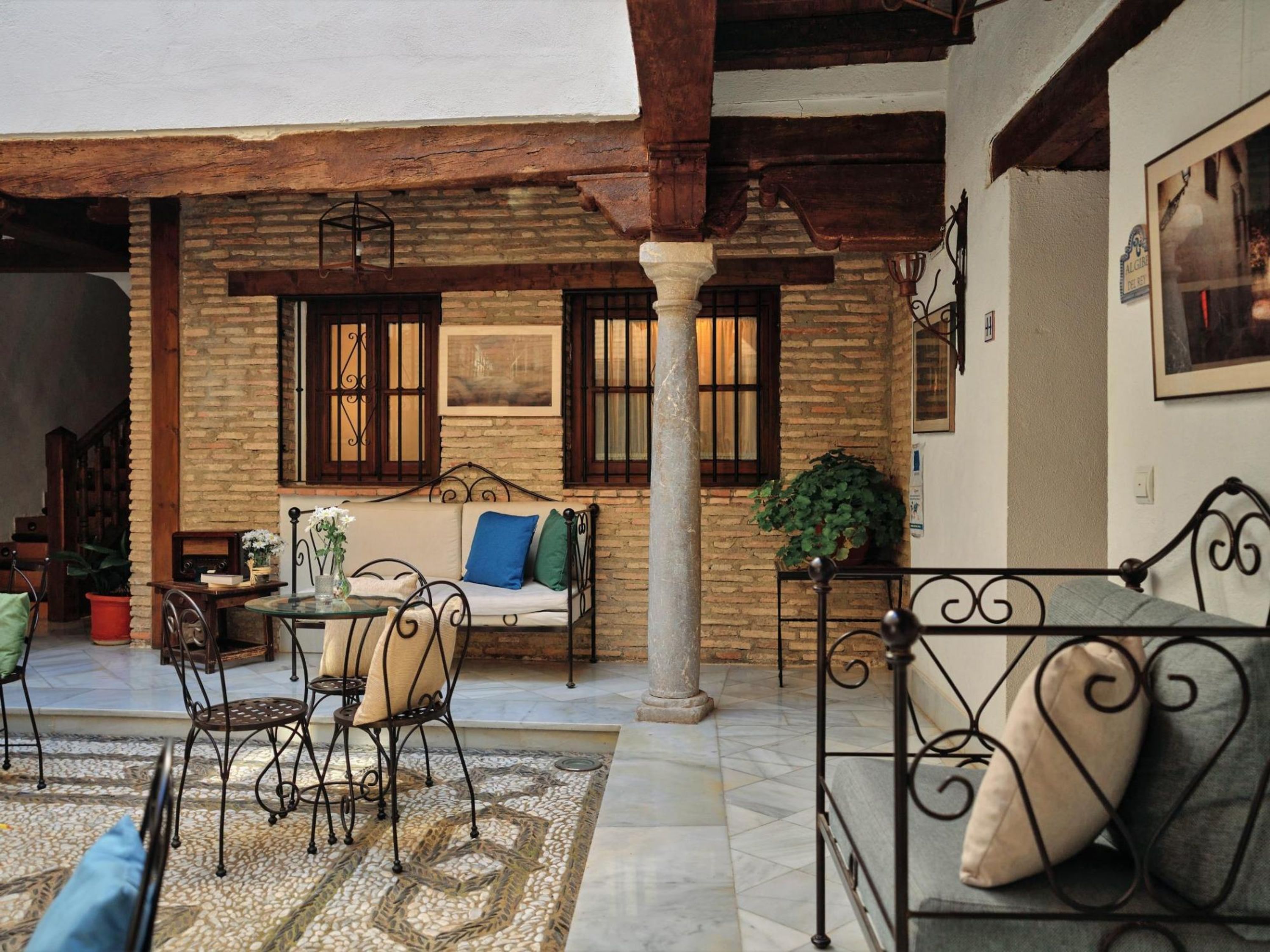 Un patio acogedor con un muro de piedra, techo de madera, banca de metal, sofá y una mesa con sillas.