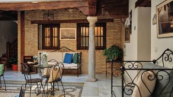 Un patio acogedor con un muro de piedra, techo de madera, banca de metal, sofá y una mesa con sillas.