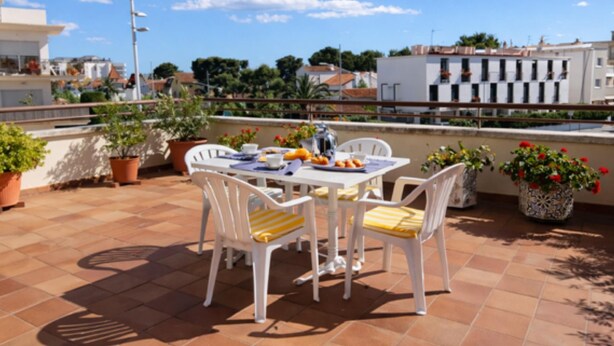A terrace with a table and chairs, potted plants, and a view of buildings. - Duplex con Zona Comunitaria Ideal Familias Coral (Sitges)