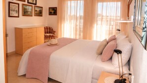 A bedroom with a bed, a dresser, a chair, and a bedside table with a lamp. - Duplex con Zona Comunitaria Ideal Familias Coral (Sitges)