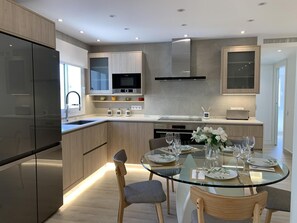 A modern kitchen with a central island, built-in appliances, and a dining area with a glass table and chairs. - Sitges Spaces Oasis Suites (Sitges)