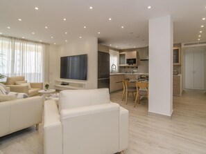 A modern living room with a sofa, TV, and dining area. - Sitges Spaces Oasis Suites (Sitges)